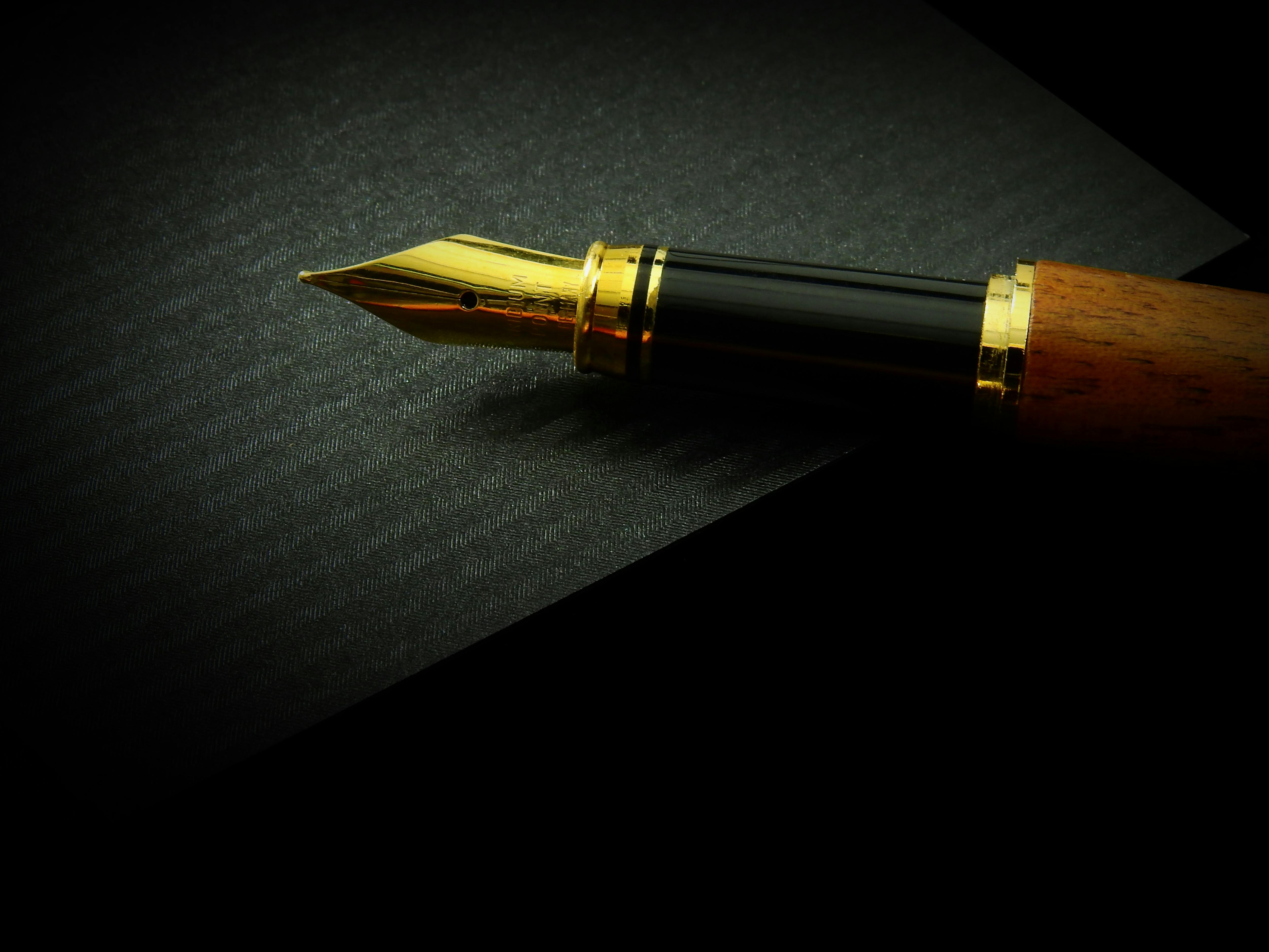 Detailed close-up of a classic fountain pen nib on textured black paper, showcasing elegance.